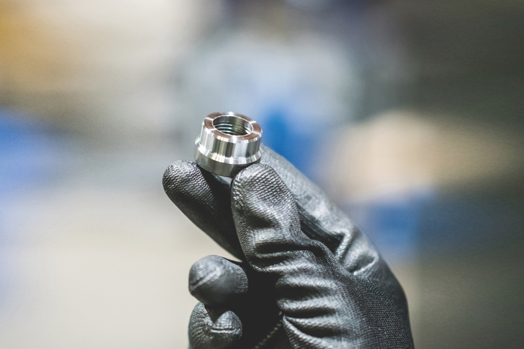 A person is holding a bolt between 3 fingers. They are also wearing thick gloves.