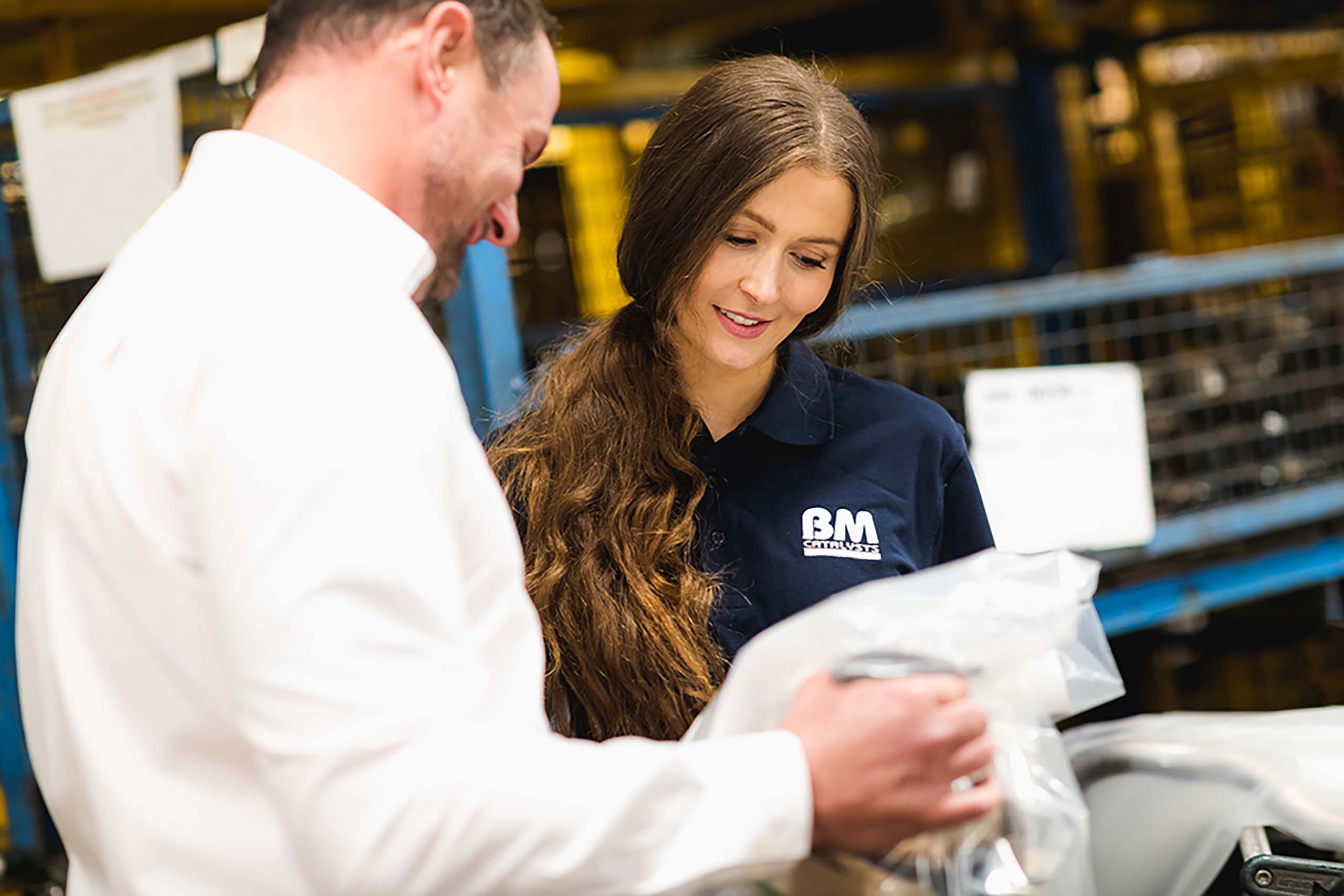 Two colleagues are looking at a packaged vehicle part in a manufactoring facility 