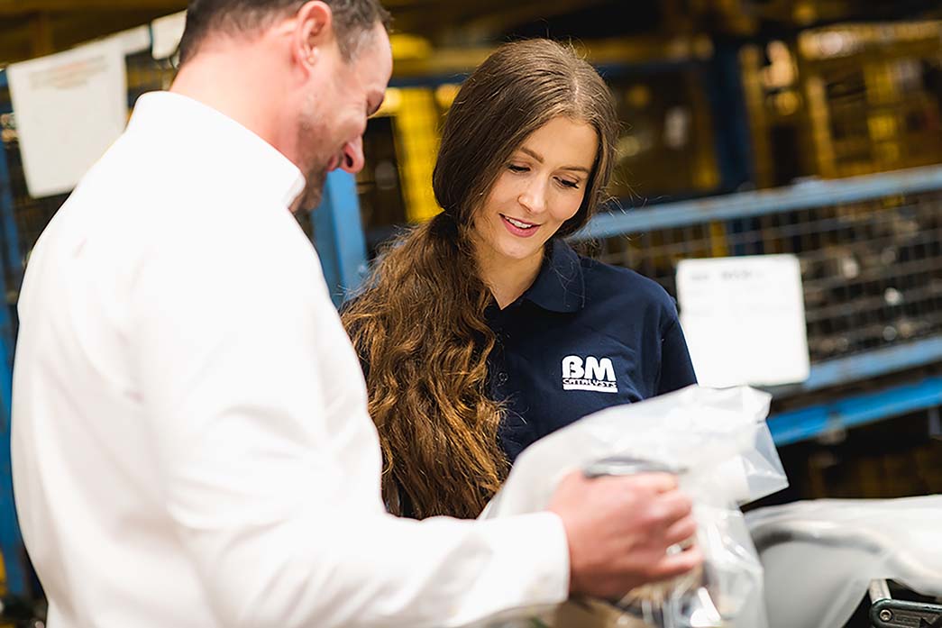 Two colleagues are looking at a packaged vehicle part in a manufactoring facility 