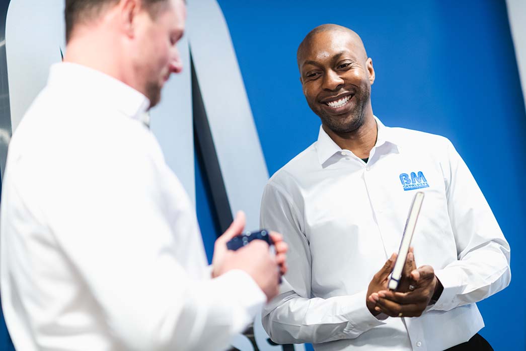 Two BM Catalysts workers are interacting. One of the men is smiling and holding a notebook while the other is hold a coffee mug.